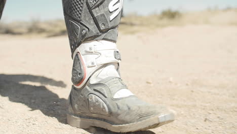 SLOW-MOTION:-A-dirt-biker-walks-in-the-desert-dirt-and-sand-in-his-dirt-biking-gear-and-uniform