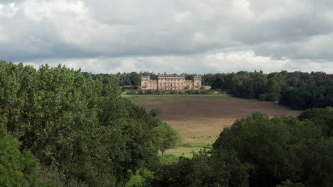 Aerial-Reveal-of-Harewood-House,-a-Country-House-in-West-Yorkshire,-through-the-Treetops-with-a-Narrow-Crop