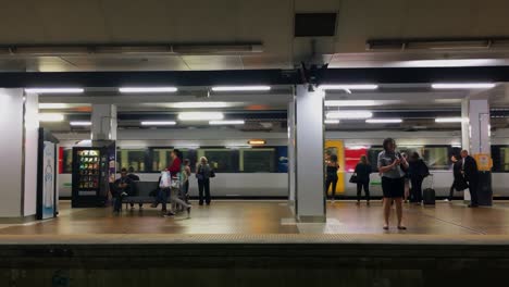 Commuters-on-a-platform-at-Central-Station,-Brisbane,-Australia,-as-a-train-pulls-in,-stops-and-opens-its-doors