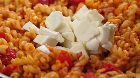 Putting-half-cup-of-mozarella-chunks-in-pan-with-fusilli-pasta-and-tomato-sauce,-close-up-shot