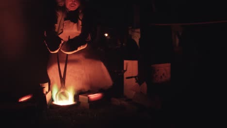 Wide-shot-of-a-medieval-blacksmith-pouring-liquid-metal-into-a-casting-mold-at-night