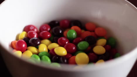 Close-Up-Pouring-Skittles-Candy-Into-White-Bowl-On-Table