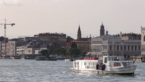El-Ferry-Turístico-En-Primer-Plano-Cambia-De-Dirección-En-El-Gran-Canal-Y-La-Ciudad-De-Venecia-Al-Fondo.