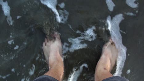 POV-shot-of-a-pair-of-feet-on-the-sand-as-the-ocean-waves-wash-over-them