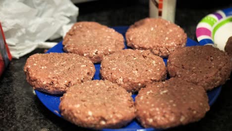 Seasoning-plant-based-burger-patties-on-a-blue-plate-for-a-summertime-barbecue-cookout,-wide-shot-60-frames-per-second-4k