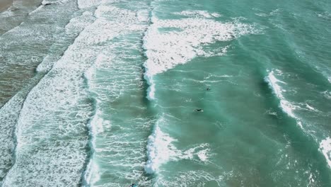 Surfers-swimming-out-through-breaking-waves.-Wide-drone-shot