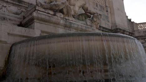 Slow-motion-tilt-up-shot-of-a-street-fountain-and-roman-sculptures-with-sun-shining-flare-in-the-Background