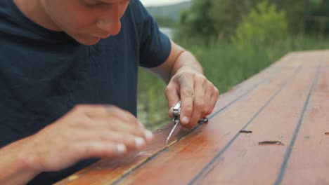 Young-man-cutting-removing-old-timber-with-knife-wooden-boat-maintenance