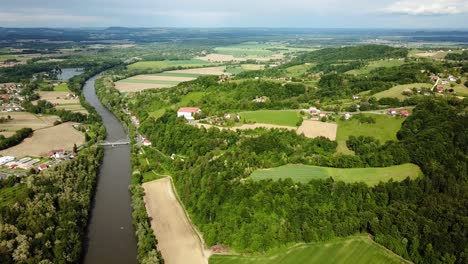 Aerial-landscape-shot-of-mura-river-and-the-surrounding-area-with-houses-and-agriculture-austria-slovenia-europe
