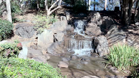 Slo-mo-of-waterfall-surrounded-by-green-foliage,-Ju-Raku-En-Japanese-Garden,-Toowoomba,-Australia