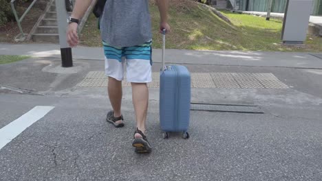 Lower-view-of-the-man-wearing-short-and-adventure-sport-sandal-while-walking-cross-the-street-in-singapore-area-with-handed-trolley-luggage