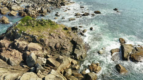 Aerial-cinematic-view-of-waves-hitting-the-coastline-rocks,-Praia-Armacao,-Florianopolis,-Santa-Catarina,-Brasil