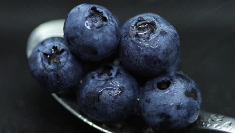 Close-up-macro-shot-of-blueberries-laying-on-a-teaspoon-of-splashed-and-spayed-water-on-a-dark-background-lying-captured-in-slow-motion