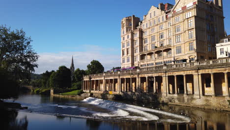 Time-Lapse-of-Pulteney-Weir-and-the-Empire-Hotel-in-Bath,-Somerset-on-Beautiful-Summer’s-Morning-with-Blue-Sky-and-Golden-Light