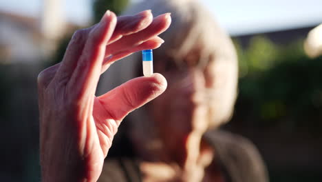 An-old-woman-holding-a-blue-prescription-medication-drug-pill-to-cure-her-cancer-illness-and-disease