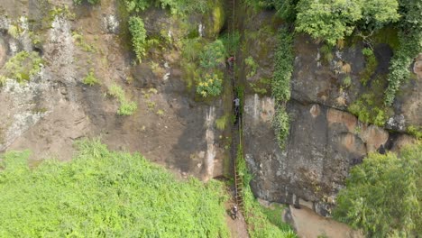 Forward-moving-aerial-shot-of-a-dangerous-ladder-climb-on-a-cliff-face-in-rural-Uganda-with-men-climbing