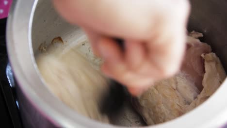 Female-hands-flipping-raw-chicken-breasts-with-a-black-pasta-picker-inside-an-old-pressure-pan---close-up