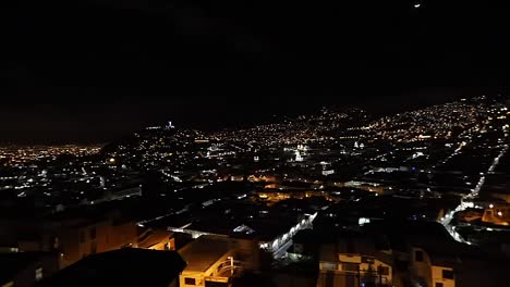 Nightime-panoramic-view-of-Quito,-Ecuador,-with-city-lights,-moon,-and-Virgen-del-Panecillo-statue