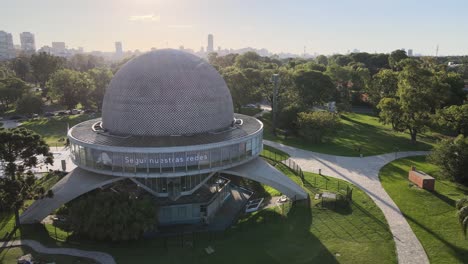 Aerial-dolly-in-over-Galileo-Galilei-Planetarium-in-Palermo-Woods-with-buildings-in-background-at-daytime,-Buenos-Aires