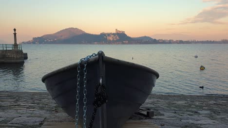Fishing-boat-out-of-water-and-tied-with-iron-chain-facing-Lake-Maggiore-and-Angera-castle,-static
