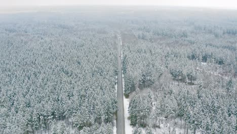 Foggy-aerial-voew-over-a-snow-covered-forest,-look-down-shot-of-a-straight-road-with-a-driving-cars-in-4K