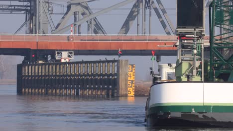 Closeup-of-waterway-corridor-leading-underneath-a-bridge-over-river-IJssel-in-the-background-with-heavy-machinery-dredging-ship-in-the-foreground-at-work