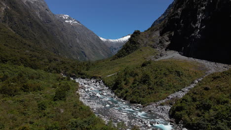 Fast-mountain-river-in-rocky-narrow-valley-below-mountain-peaks-in-Fiordland-Southland,-New-Zealand