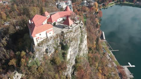 Aerial-shot-of-a-castle-near-a-lake-perched-on-a-high-rock-in-the-mountains-of-Slovenia,-Lake-Bled