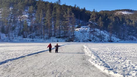 Toddler-girls-walking-and-stumbling-together-on-ski-and-ice-skates---happy-young-friends-at-snow-covered-frozen-lake