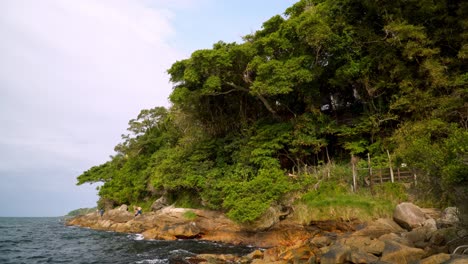 Sea-waves-hitting-a-rocky-shore-near-a-dense-green-forest-in-Bombas-and-Bombinhas-beaches,-Brazil
