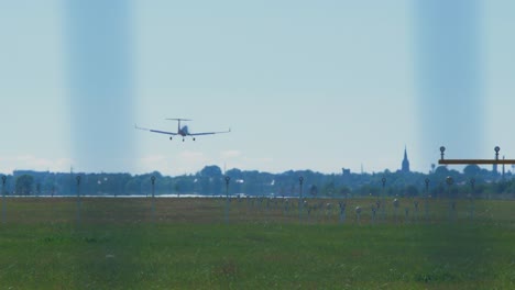 Small-white-training-airplane-with-propeller-engines-landing-at-airport-in-sunny-summer-day,-medium-shot-from-a-distance