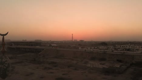 Aerial-View-Of-Mosque-Minaret-Near-Highway-In-Karachi-Against-Orange-Yellow-Sunset-Skies