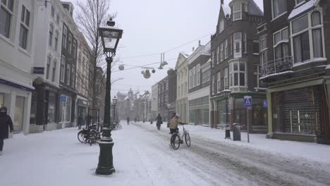 People-walking-and-cycling-on-snowy-Breestraat-road-in-Leiden-city,-Netherlands
