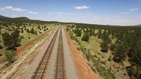 Aerial-pull-away-from-a-single-man-standing-along-the-parallel-train-tracks​-near-Williams,-Arizona