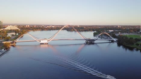 Aerial-view-of-a-Matagarup-Bridge-in-Perth,-Western-Australia-with-boat-going-through-waves-on-Swan-River