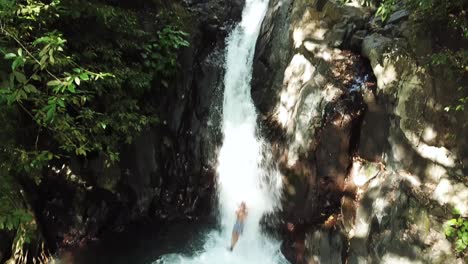 Panning-down-drone-shot-following-someone-sliding-down-the-natural-waterslide-at-AlingAling-Waterfall-in-Bali,-Indonesia