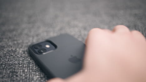 Close-up-of-hand-picking-up-dark-new-iPhone-from-soft-grey-surface