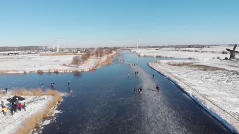 Ice-skaters-on-frozen-Netherlands-canal-in-dutch-countryside,-aerial-winter-view