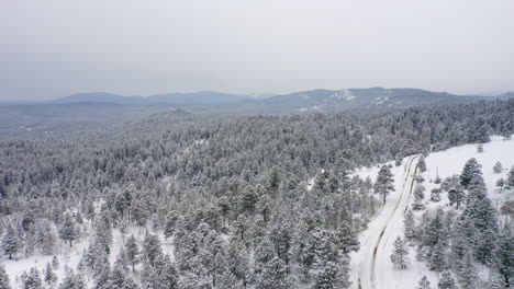 Aerial-drone-view-of-snowy-unplowed-back-roads-in-Colorado-surrounded-by-snow-and-ice-covered-pine-tree-forests-after-winter-storm
