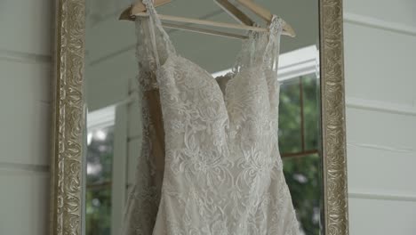 Gorgeous-pan-of-a-white-wedding-dress-hanging-in-a-mirror-which-is-reflecting-the-image-of-the-woods-outside-teh-window-in-a-well-lit-white-room-at-Le-Belvédère-in-Wakefield,-Quebec,-Canada