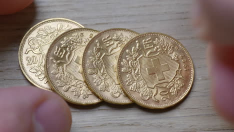 Monedas-Suizas-Doradas-Brillantes-Apiladas-A-Mano-Masculina-Sobre-Una-Mesa-De-Madera,-De-Cerca