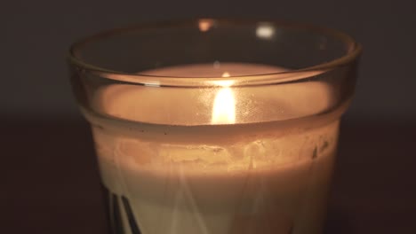 Close-macro-view-of-glass-white-wax-candle-and-bright-yellow-flame-at-home