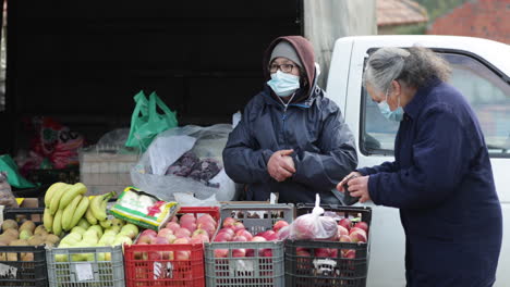 A-Woman-Wearing-Winter-Clothes-And-Face-Mask-Merchandise-Variety-Of-Fruits-On-Stall-At-Sidewalks-In-Leiria,-Portugal