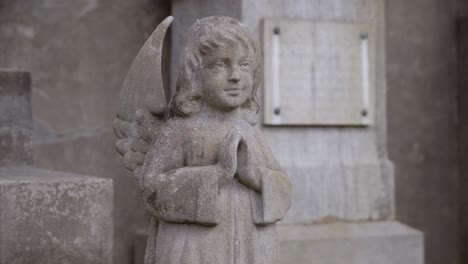 Pequeño-Y-Lindo-ángel-De-Piedra-Rezando-Frente-A-Una-Lápida-En-El-Cementerio