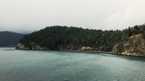 Rocky-gray-island-covered-with-green-trees-in-the-Trincomali-channel-on-a-cloudy-day-in-Canada