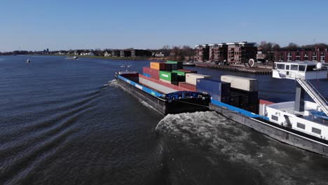 Cargo-Barge-With-Shipping-Containers-Crossing-Noord-River-And-Passing-By-Town-Of-Hendrik-Ido-Ambacht-In-Netherlands