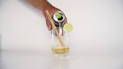 Hand-pours-Monster-Energy-drink-to-glass-with-organic-straw-on-white-background