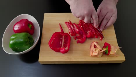 Male-Hands-Slicing-Red-And-Green-Bell-Pepper-On-A-Wooden-Chopping-Board---high-angle-shot,-close-up