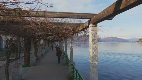 First-person-view-walking-under-porch-along-Arona-lakeside,-Italy