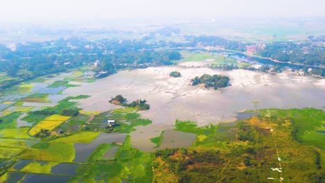 Aerial-landscape-view-of-rural-village-with-cultivated-wetland-and-small-river,-zoom-in-shot
